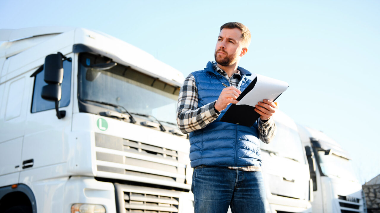 Is a TMS worth the investment? Featured image showing fleet manager inspecting a row of trucks using a notepad