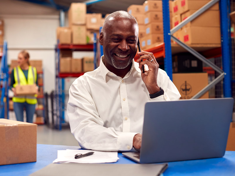 Logistics manager smiling at desk in warehouse after realising TMS is worth the investment