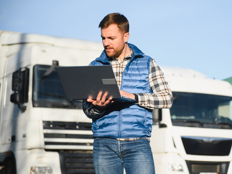 Advantages of implementing a TMS showing fleet manager using laptop in front of a row of trucks