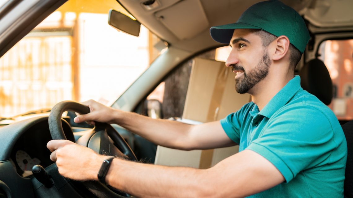 Male-Delivery-Worker-in-Teal-Shirt-Driving-Delivery-Van-During-Times-of-Rising-Fuel-Prices
